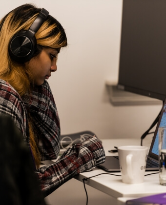 A woman sitting at a desk using a laptop and wearing headphones