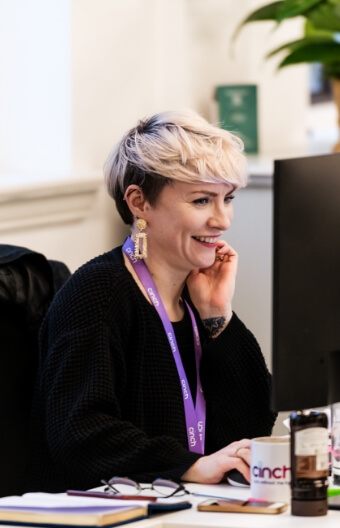 A smiling woman sat at a desk using a computer